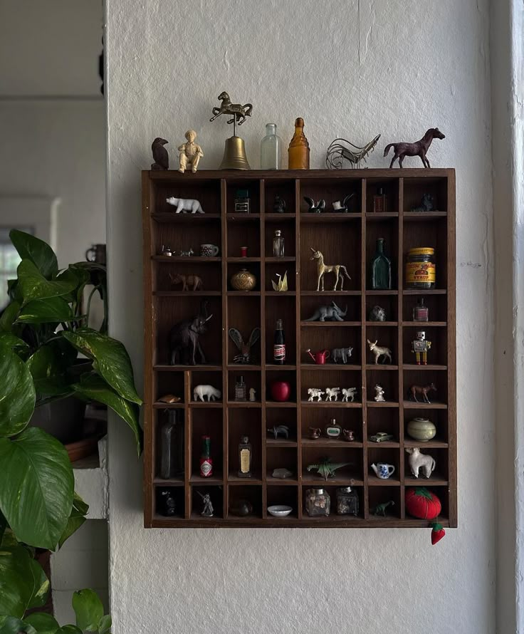 a wooden shelf filled with figurines on top of a wall next to a potted plant