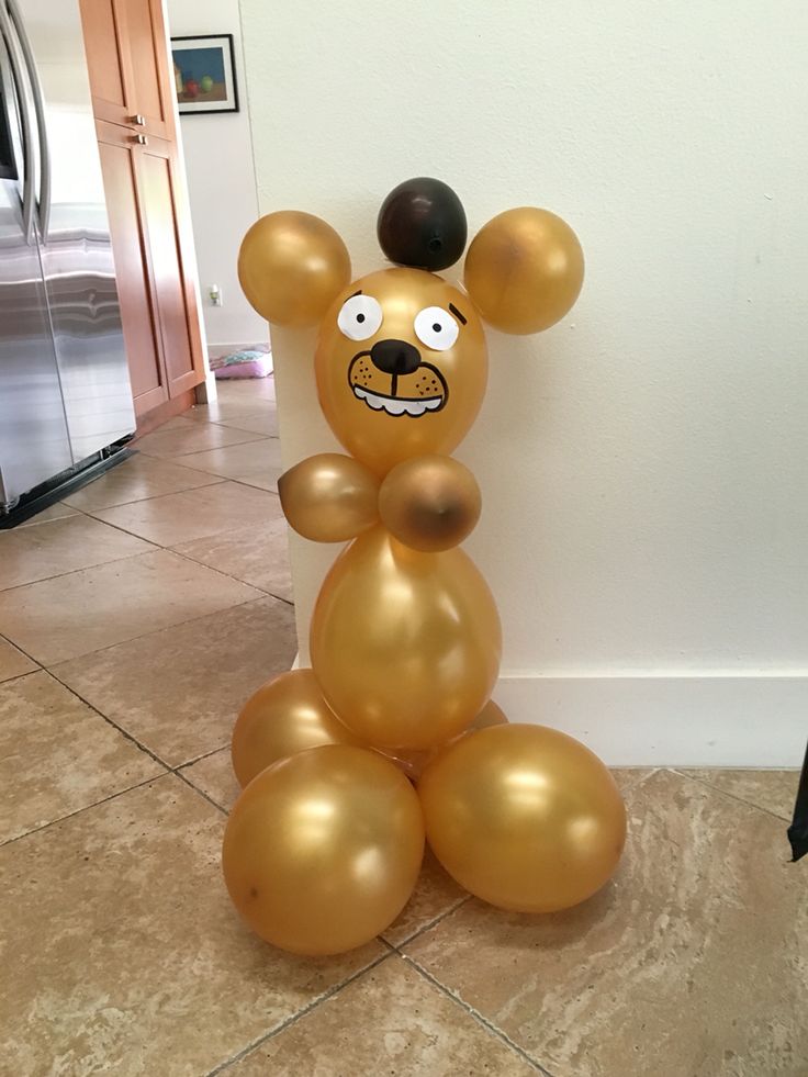 a gold balloon shaped like a bear sitting on the floor next to a wall and refrigerator