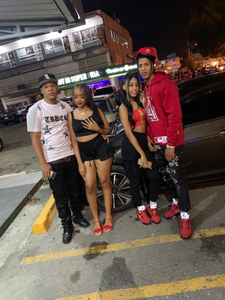 four young people standing in front of a car at night with one person wearing red shoes