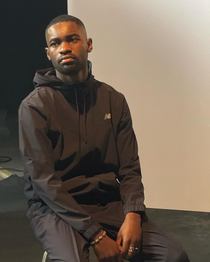 a man sitting on top of a chair wearing a black hoodie and sweatpants