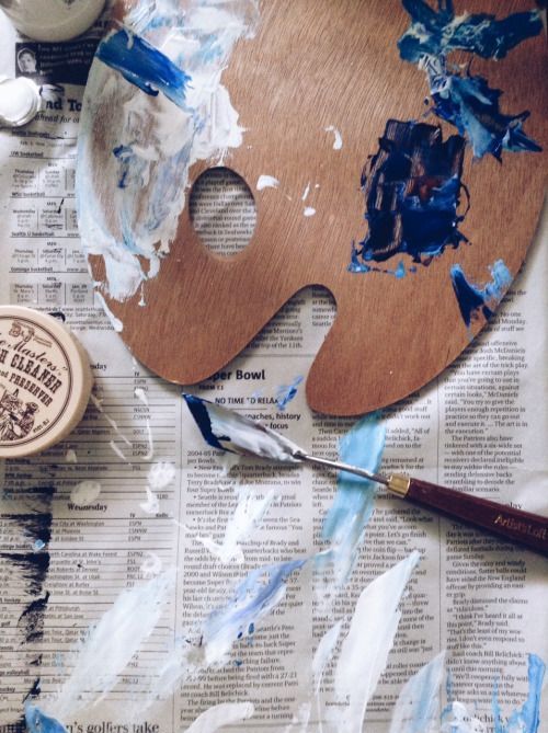 a wooden mask sitting on top of a newspaper next to paintbrushes and glue