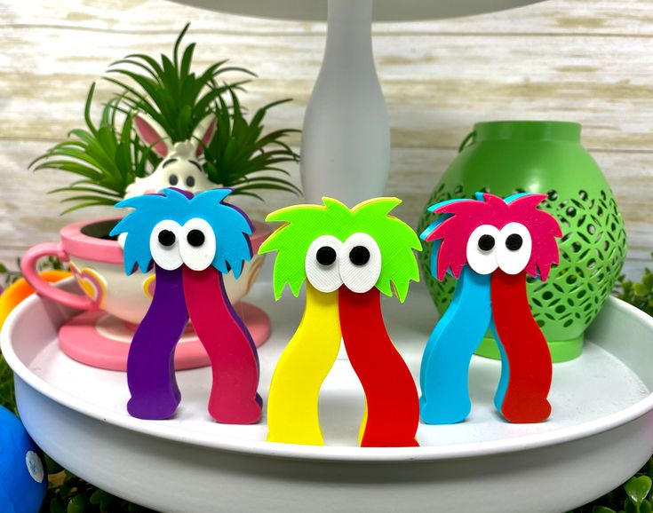 three colorful toy figures sitting on top of a white plate next to a potted plant