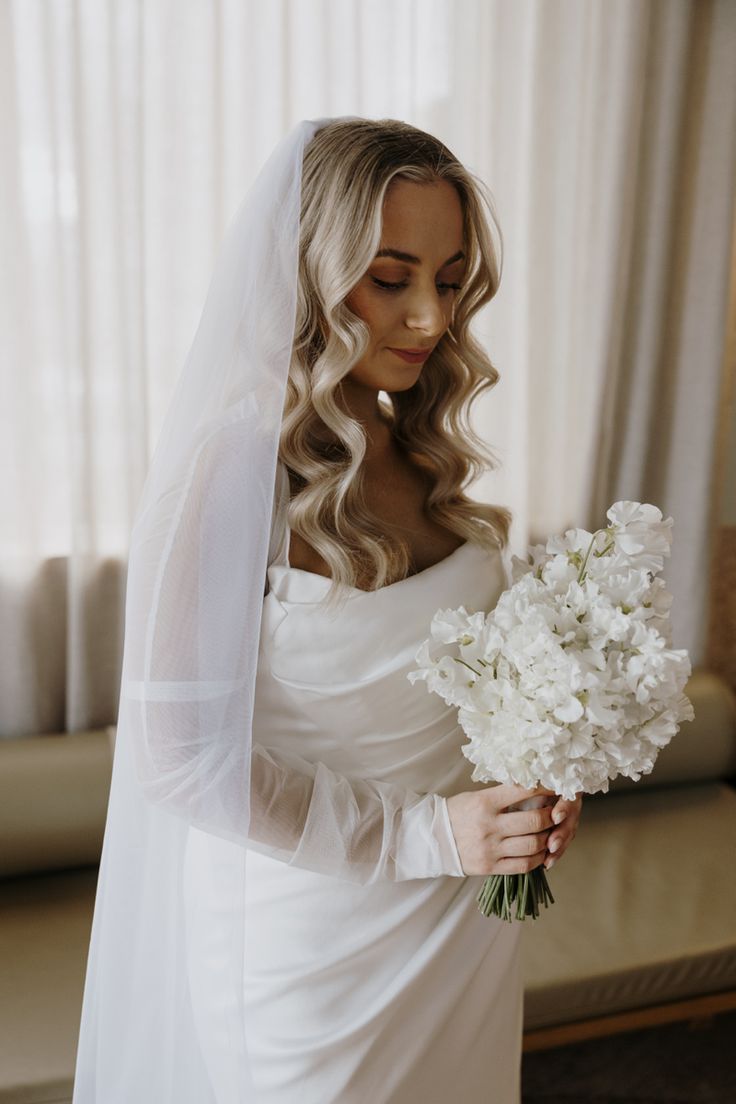 a woman in a wedding dress holding a bouquet of white flowers and wearing a veil