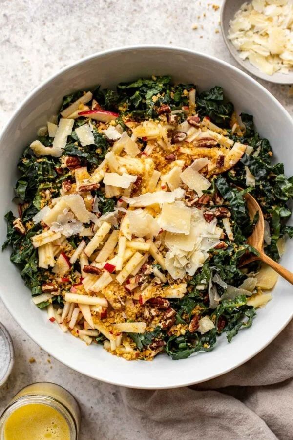 a white bowl filled with pasta and greens next to two glasses of orange juices