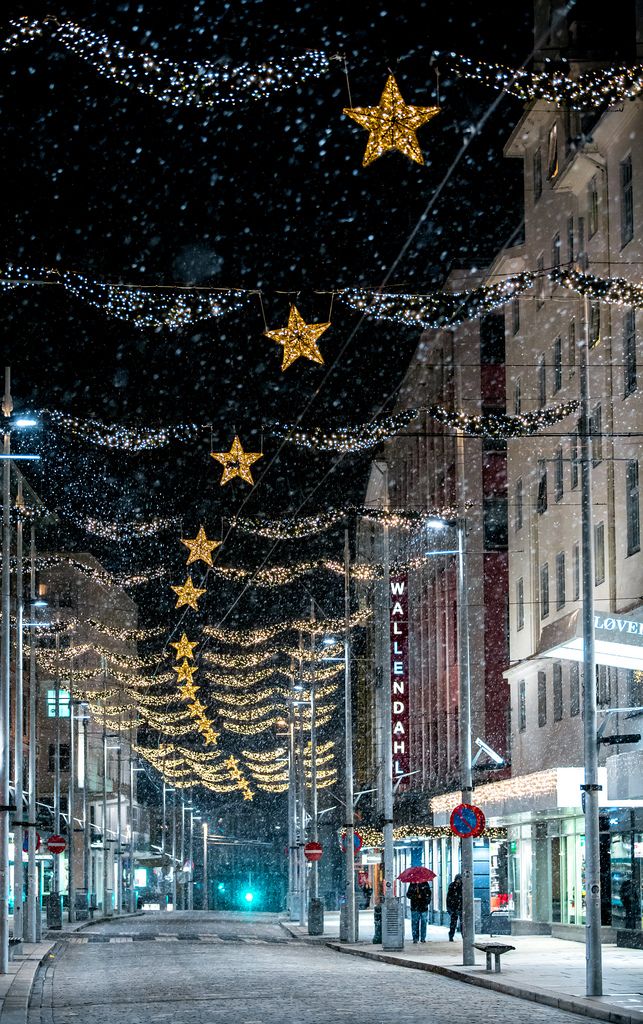 an empty city street is lit up with christmas lights and garlands on the buildings