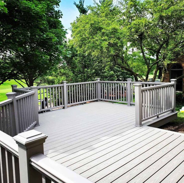 a wooden deck with white railings and trees in the back ground, surrounded by green grass