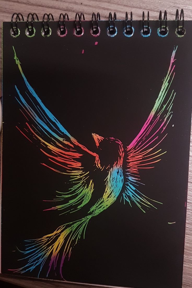 a spiral notebook with an image of a bird painted on the cover and colored pencils next to it