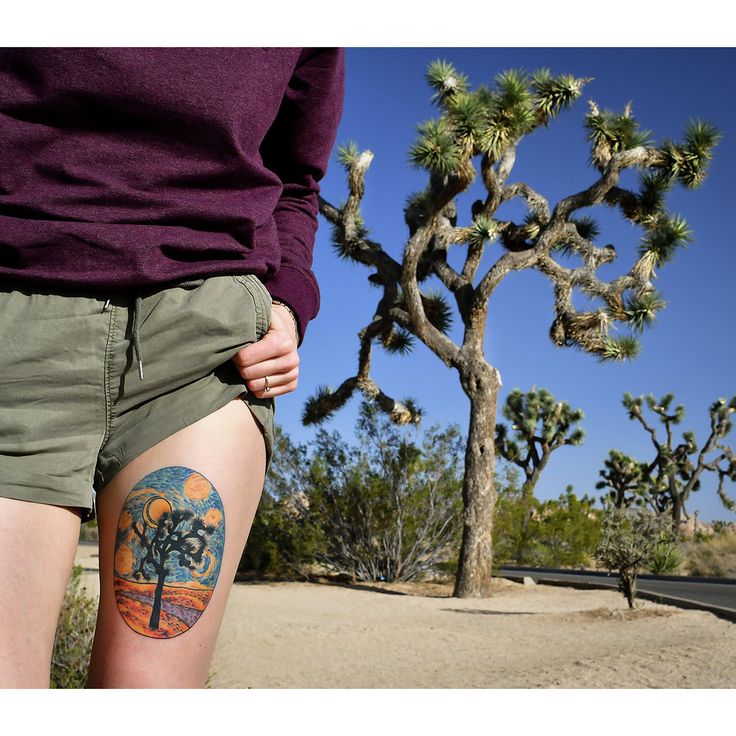 a person standing in front of a tree with tattoos on their butts and legs