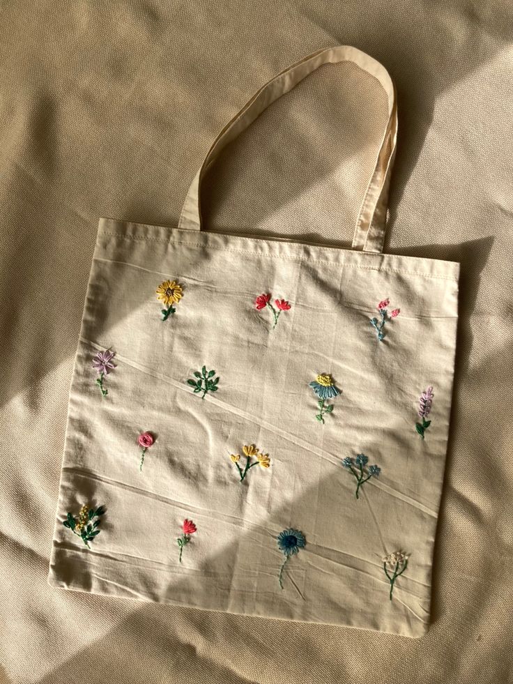 a white bag with colorful flowers on it sitting on a bed next to a pillow