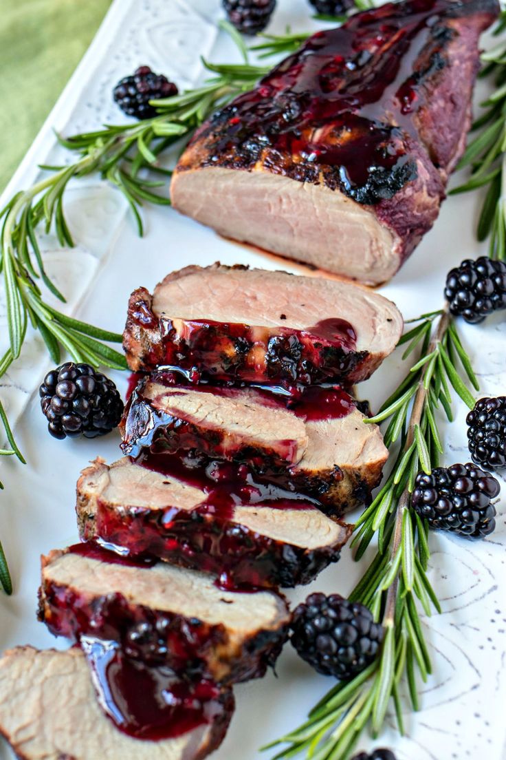 sliced pork with blackberry sauce and rosemary garnish on a white platter next to blackberries