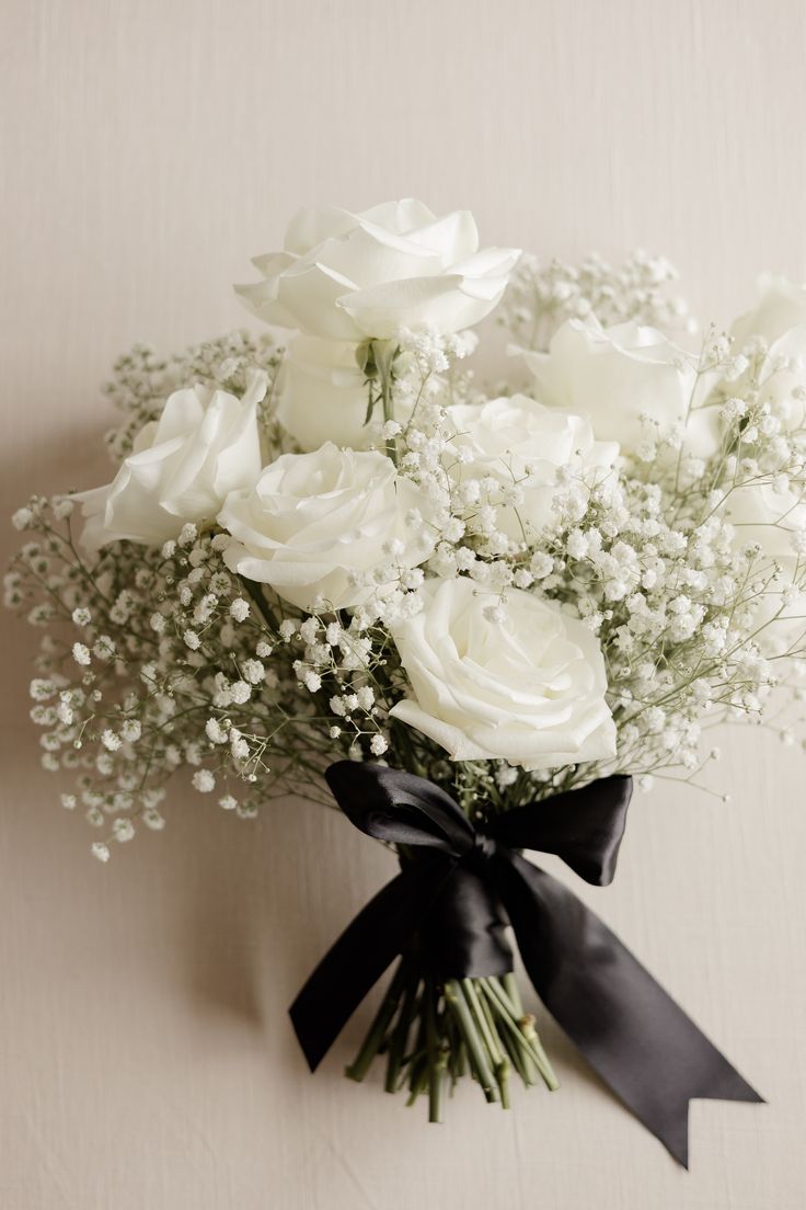 white roses and baby's breath tied together with a black ribbon on a wall