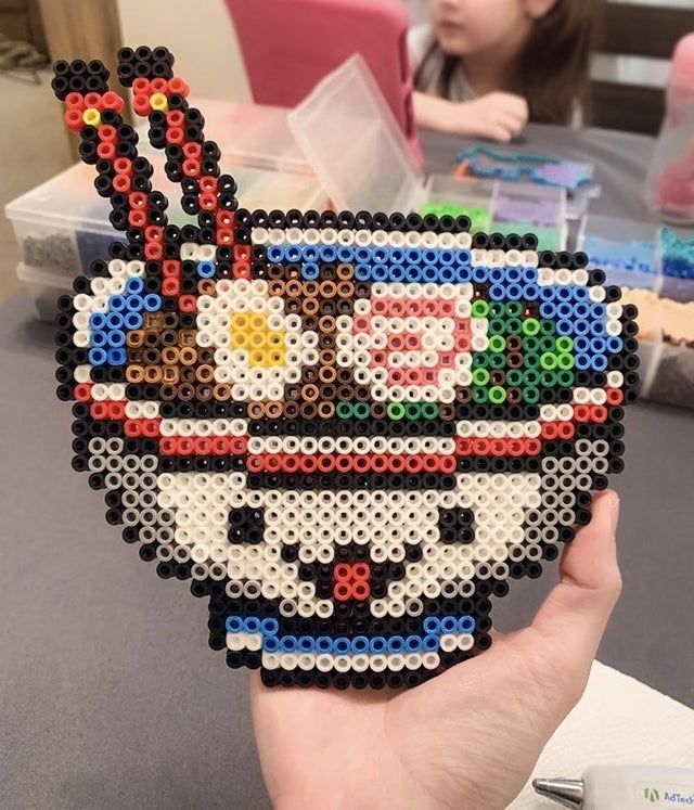 a person holding up a piece of art made out of legos in front of a table