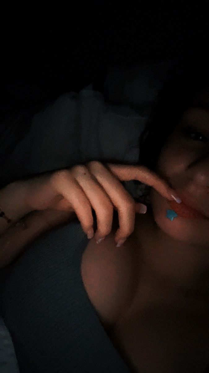 a woman laying in the dark with her hand on her chest and nails painted blue