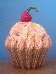 a knitted cupcake sitting on top of a wooden table next to a blue wall