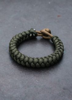 a green and black rope bracelet sitting on top of a gray floor next to a brown string