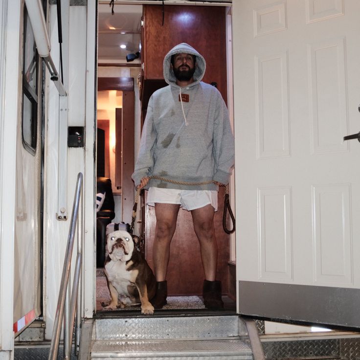 a man standing in the doorway of a moving truck with his dog sitting next to him