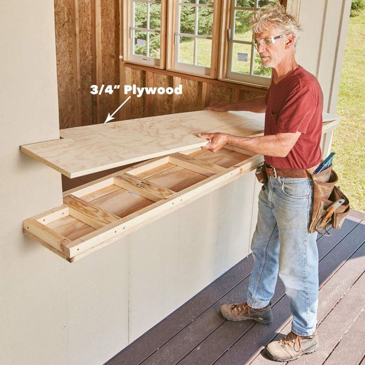 a man is standing on the porch with some wood in front of him and pointing at it