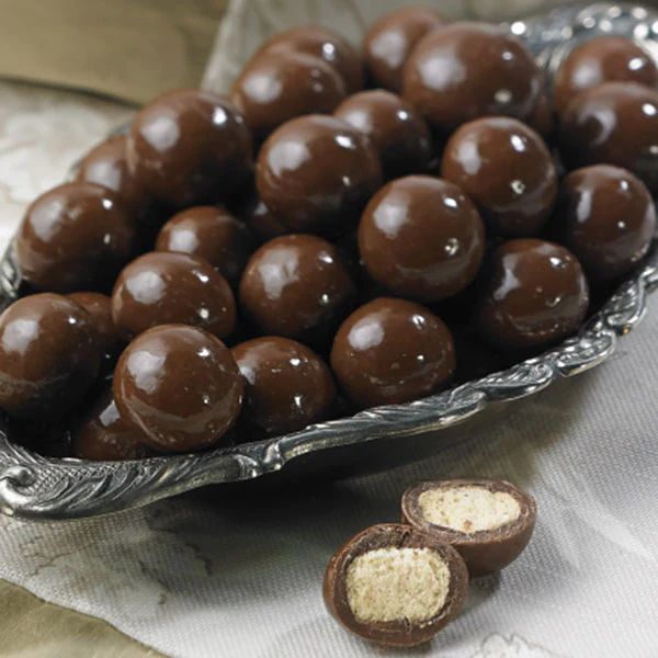 chocolate covered candies in a metal bowl on a table with two spoons next to it