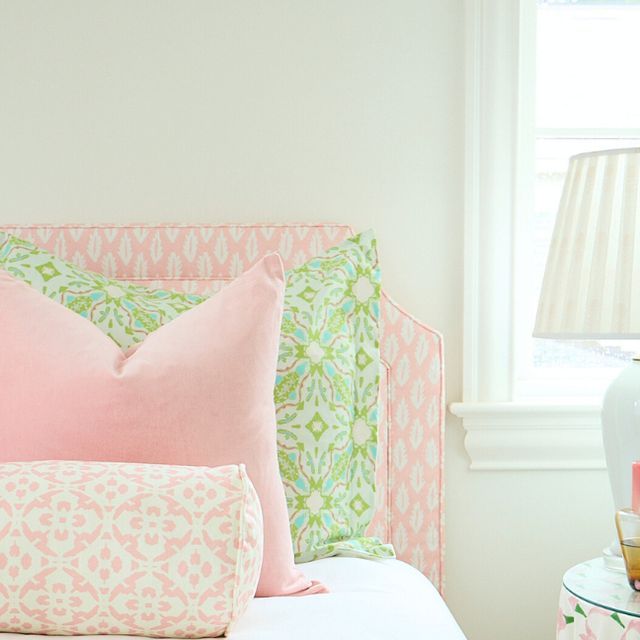 a bed with pink and green pillows on top of it's headboard next to a window