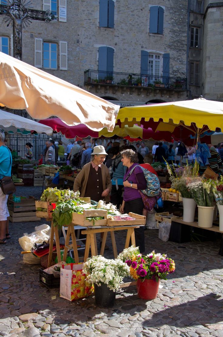 people shopping at an outdoor market with umbrellas and tables full of flowers on cobblestone pavement