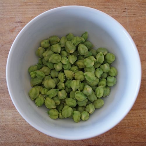 a white bowl filled with green sprouts on top of a wooden table