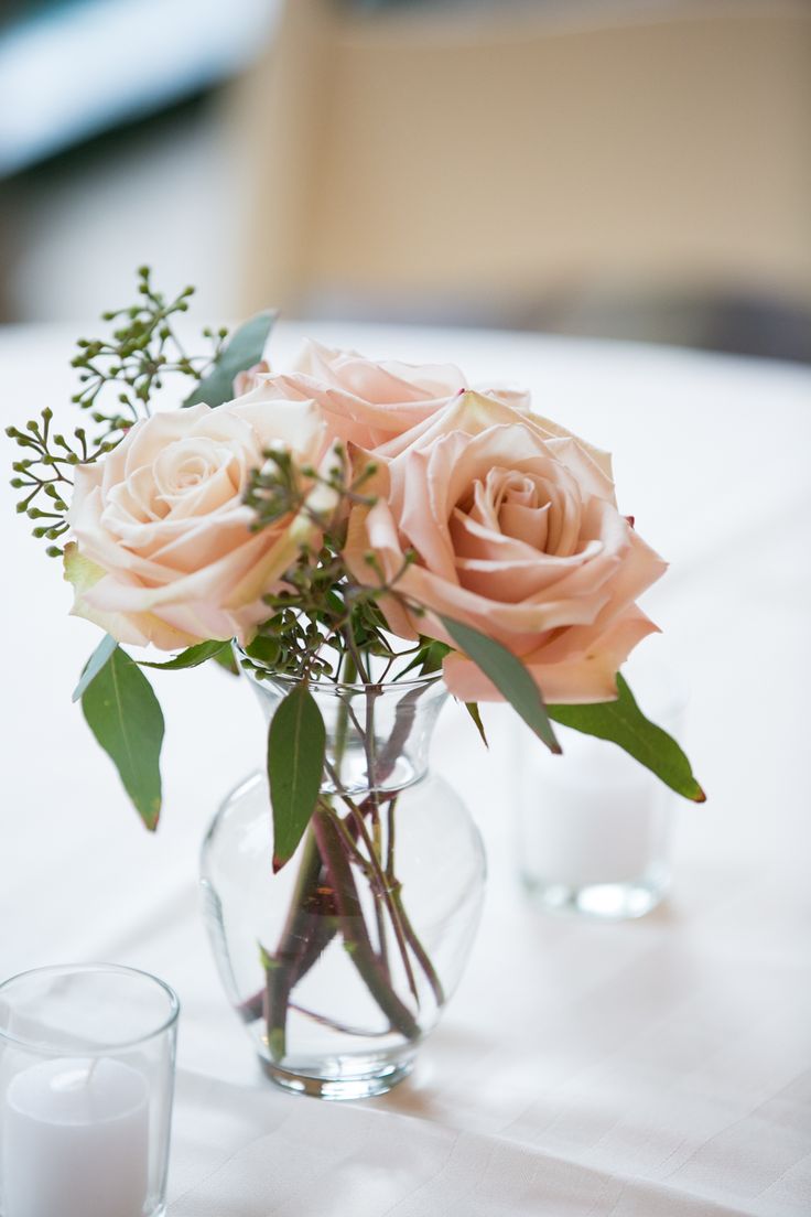 two vases filled with pink roses and greenery on a white table cloth covered table