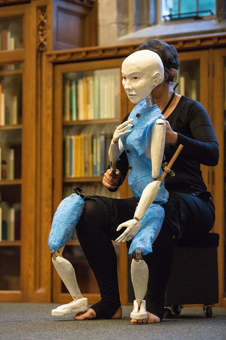 a woman sitting next to a mannequin in front of a bookshelf