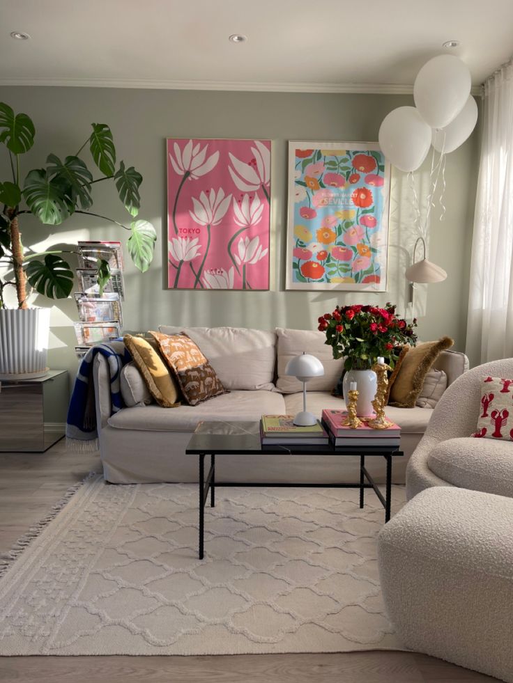 a living room filled with white furniture and paintings on the wall above it's windows