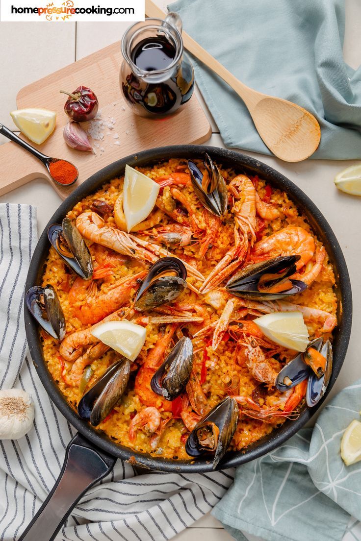 seafood paella in a skillet with lemon wedges and garlic on the side