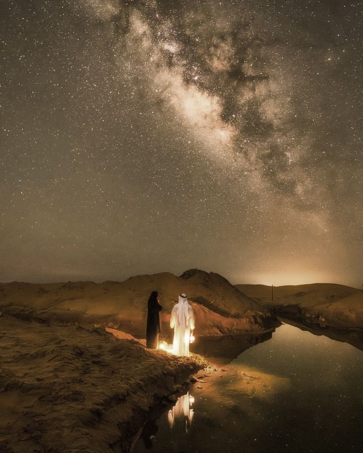 two people standing in front of a lake under a night sky with stars above them