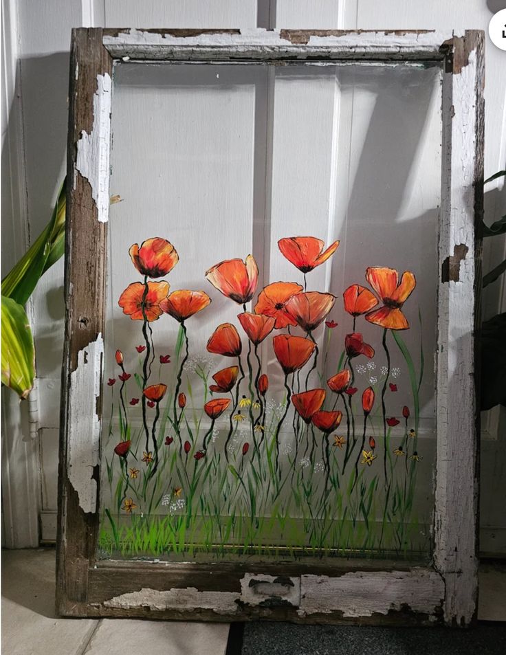 an old window decorated with red flowers and green grass in front of a white wall