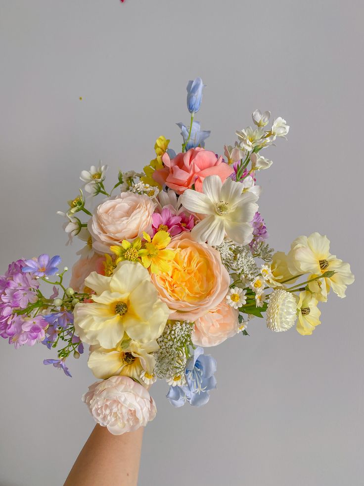 a hand holding a bouquet of flowers on a gray background with white and blue accents