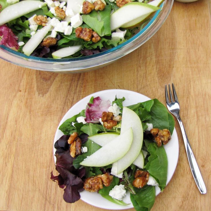 a salad with apples and walnuts in it on a white plate next to a fork