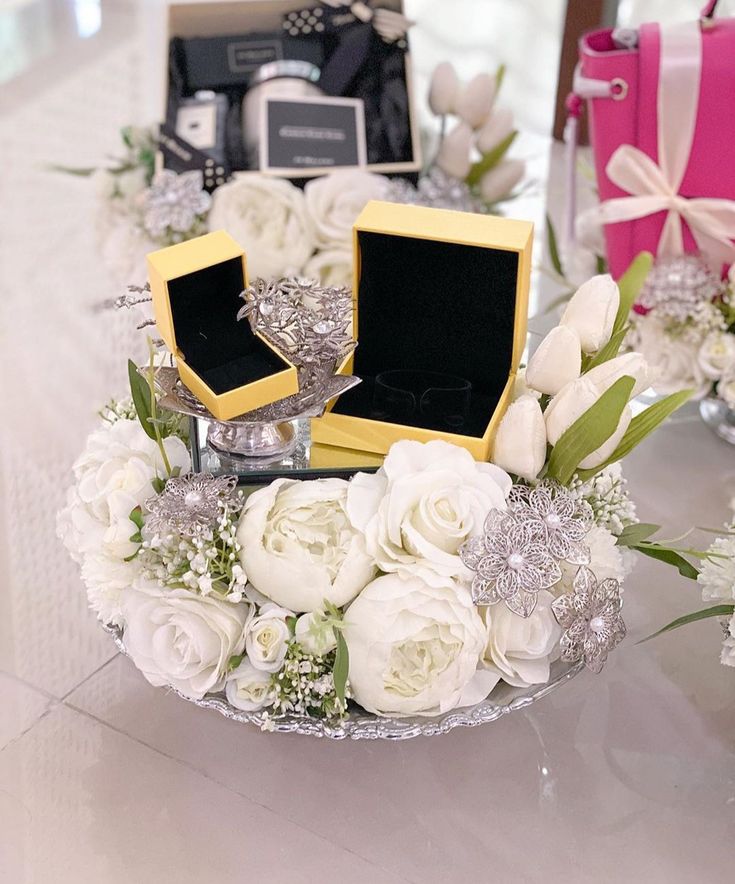 a table topped with white flowers and boxes filled with wedding rings on top of it