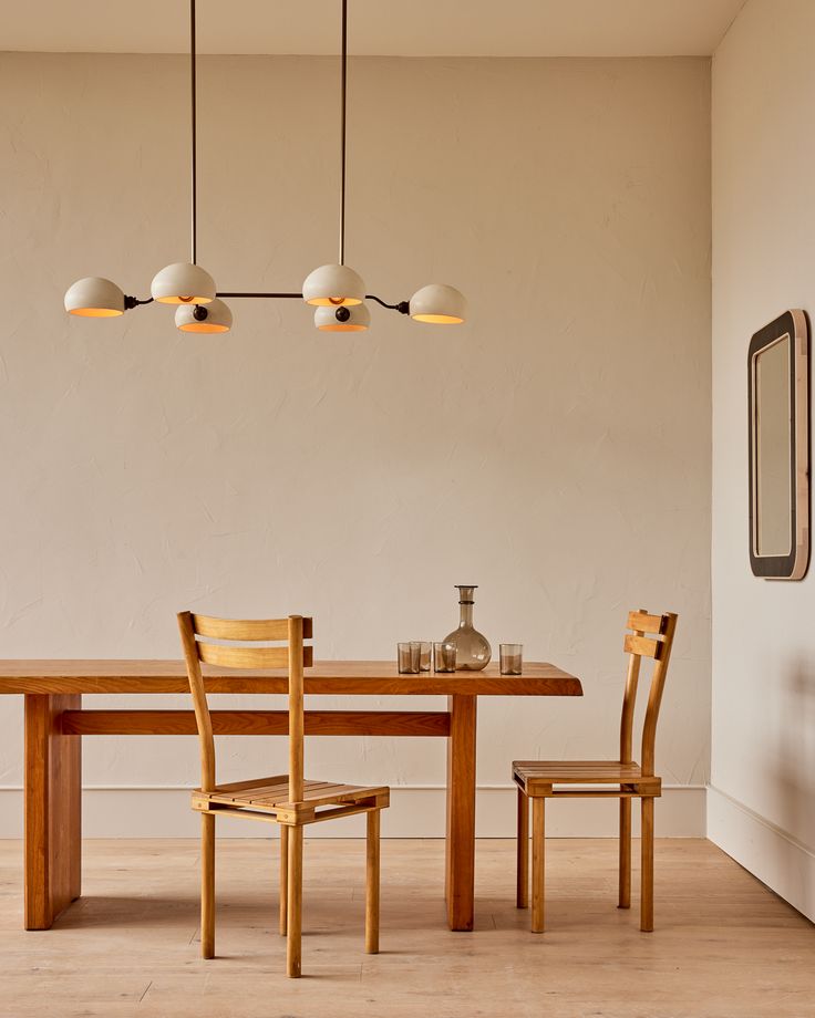 a wooden table with two chairs and three lights hanging from it's ceiling in a dining room