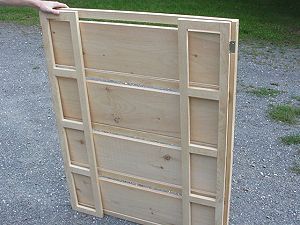 a person is holding up a wooden bookcase on the ground with grass in the background