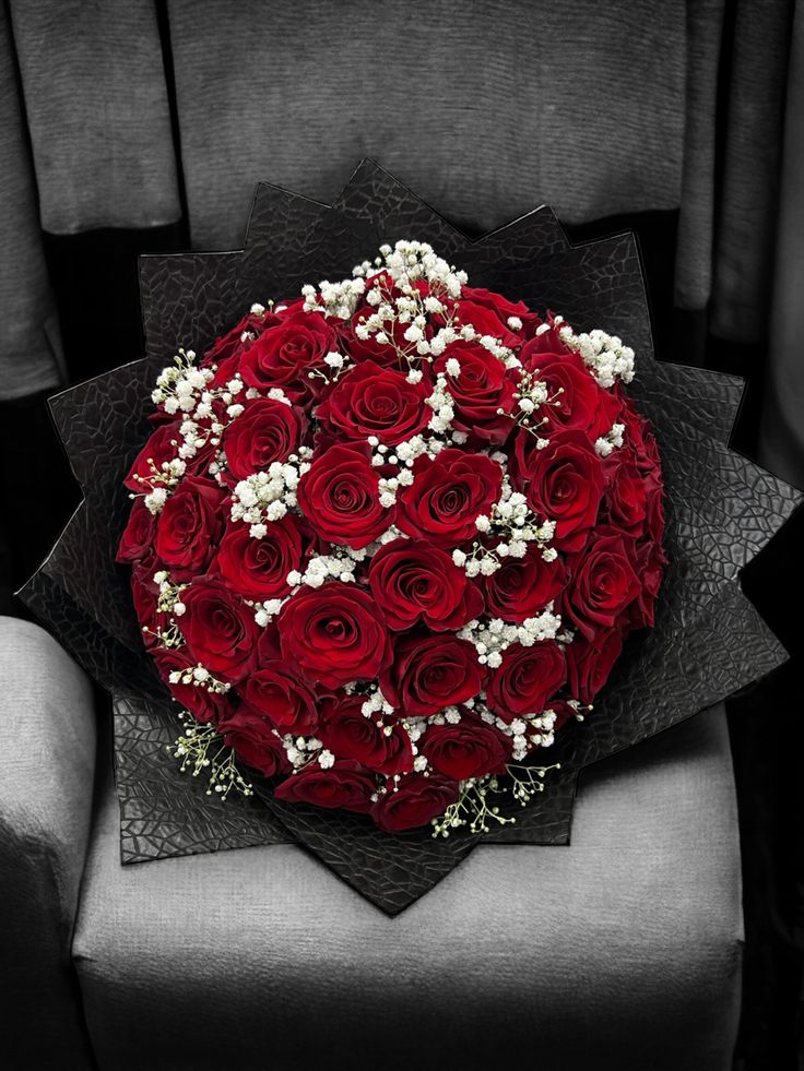 a bouquet of red roses sitting on top of a gray chair with baby's breath