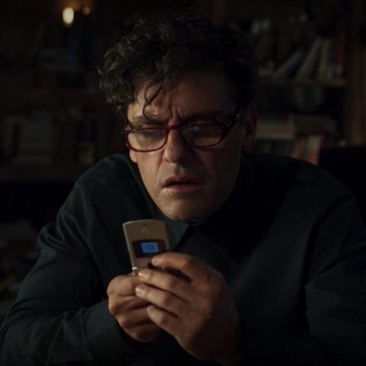 a man wearing glasses looking at his cell phone in the dark with an intense look on his face