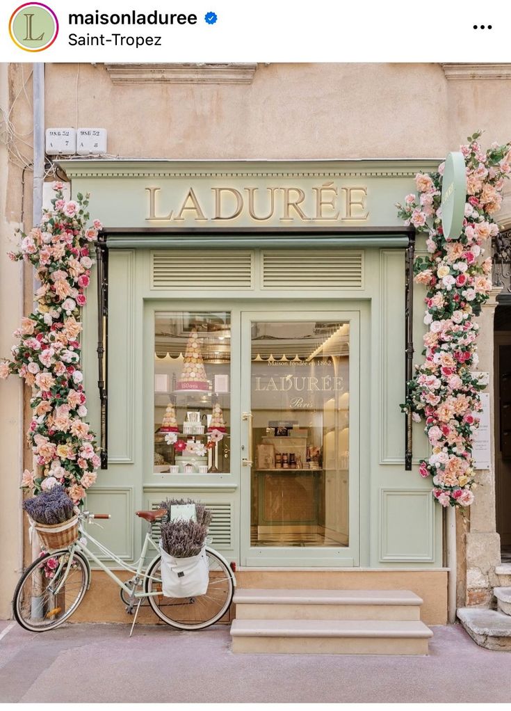 a bicycle is parked in front of a store with pink flowers on the outside and green doors