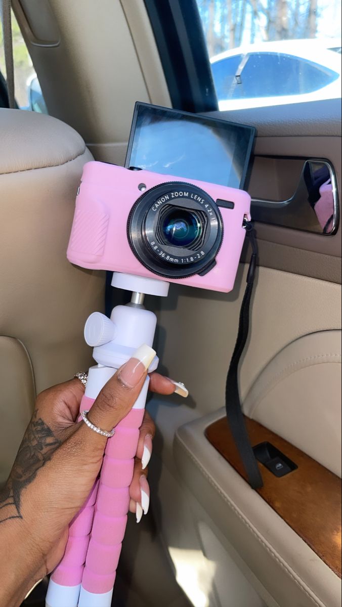 a person holding a pink camera in the back seat of a car