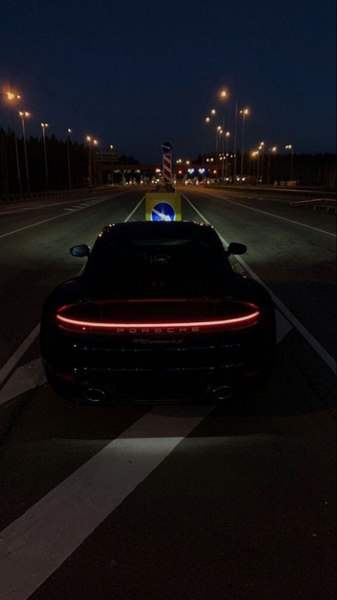 a black sports car is parked on the side of the road at night with its lights on