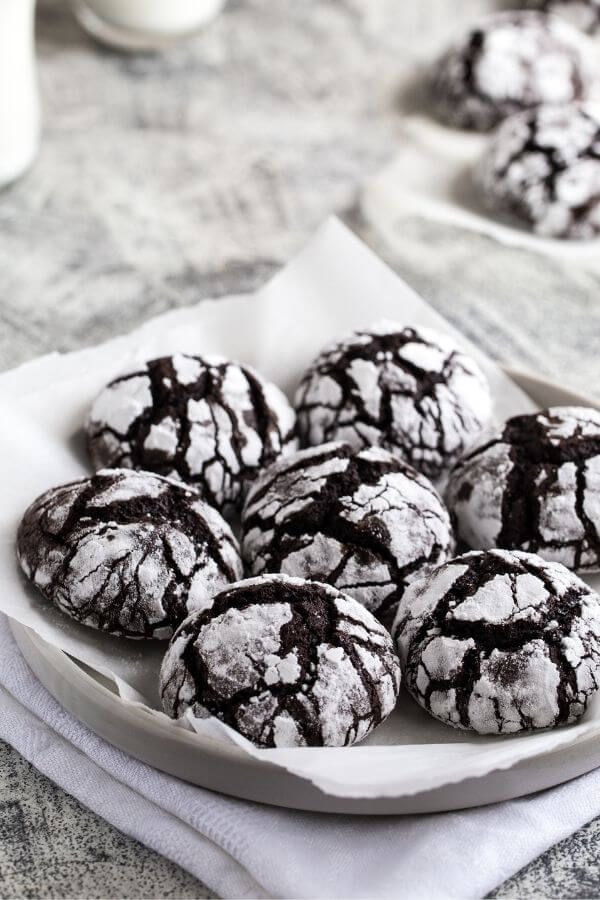 chocolate crinkle cookies sitting on top of a white plate covered in powdered sugar