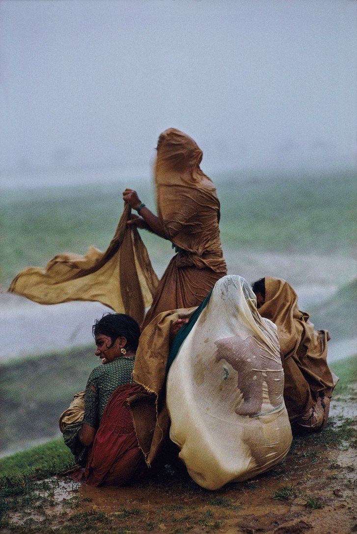 two people sitting on the ground next to each other and one is holding an umbrella