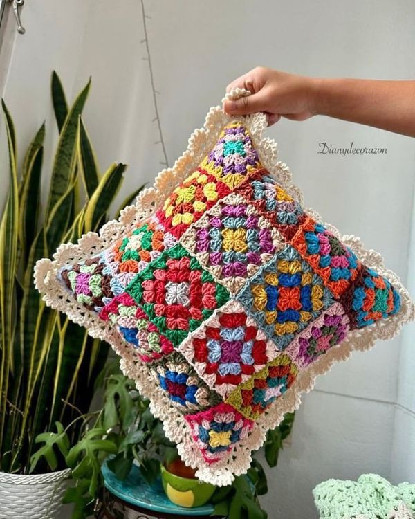 a crocheted pillow is being held by a woman's hand over a potted plant