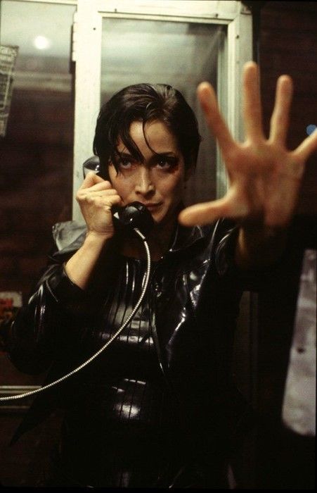 a man in black leather jacket talking on a cell phone with two hands raised up