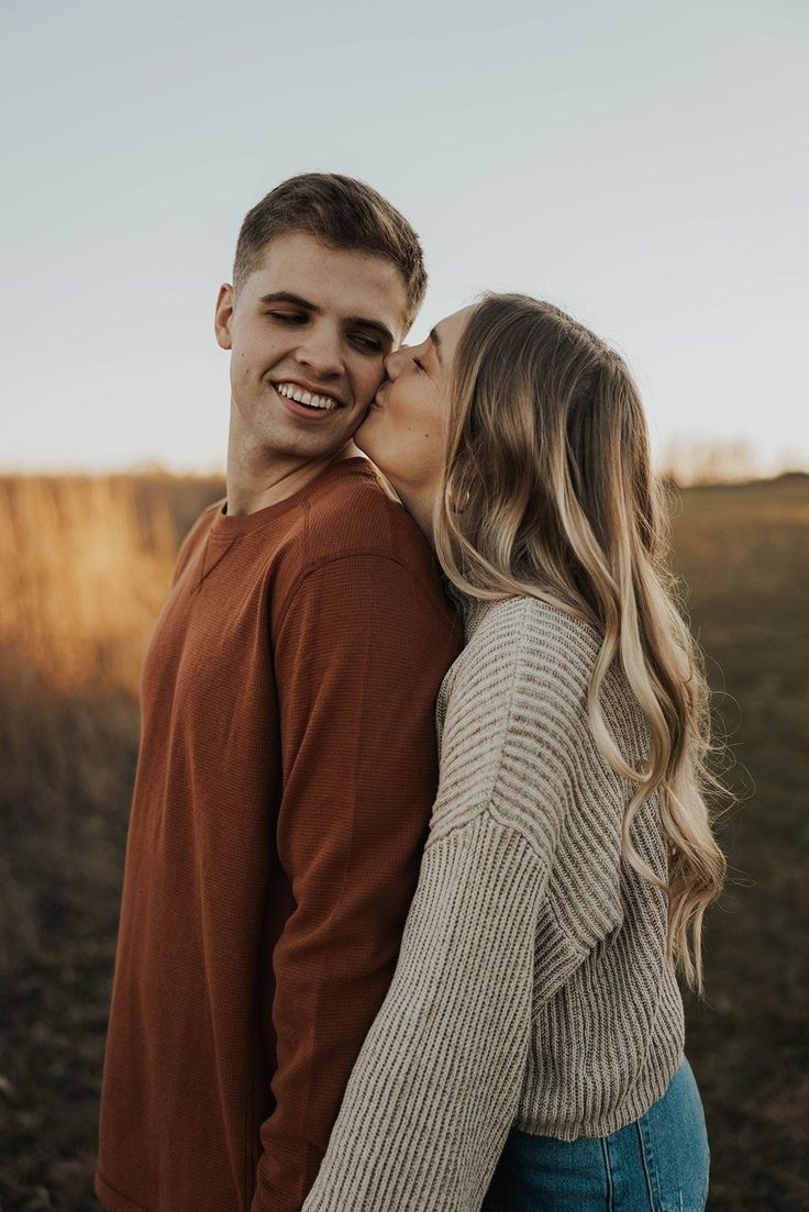 a young man and woman kissing each other in the middle of an open field at sunset