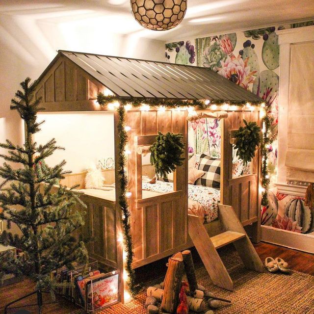 a child's play house with christmas lights and decorations on the roof, next to a tree