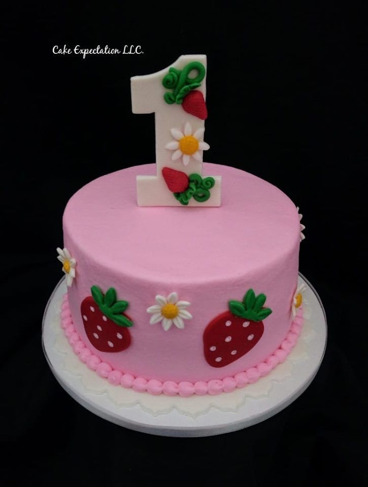 a pink birthday cake with strawberrys and daisies on the top, number one