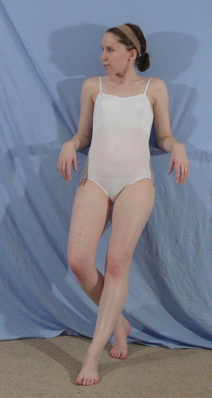 a woman standing in front of a blue backdrop wearing a white one piece swimsuit