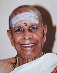 an old man with white hair and a red cross on his forehead smiles at the camera